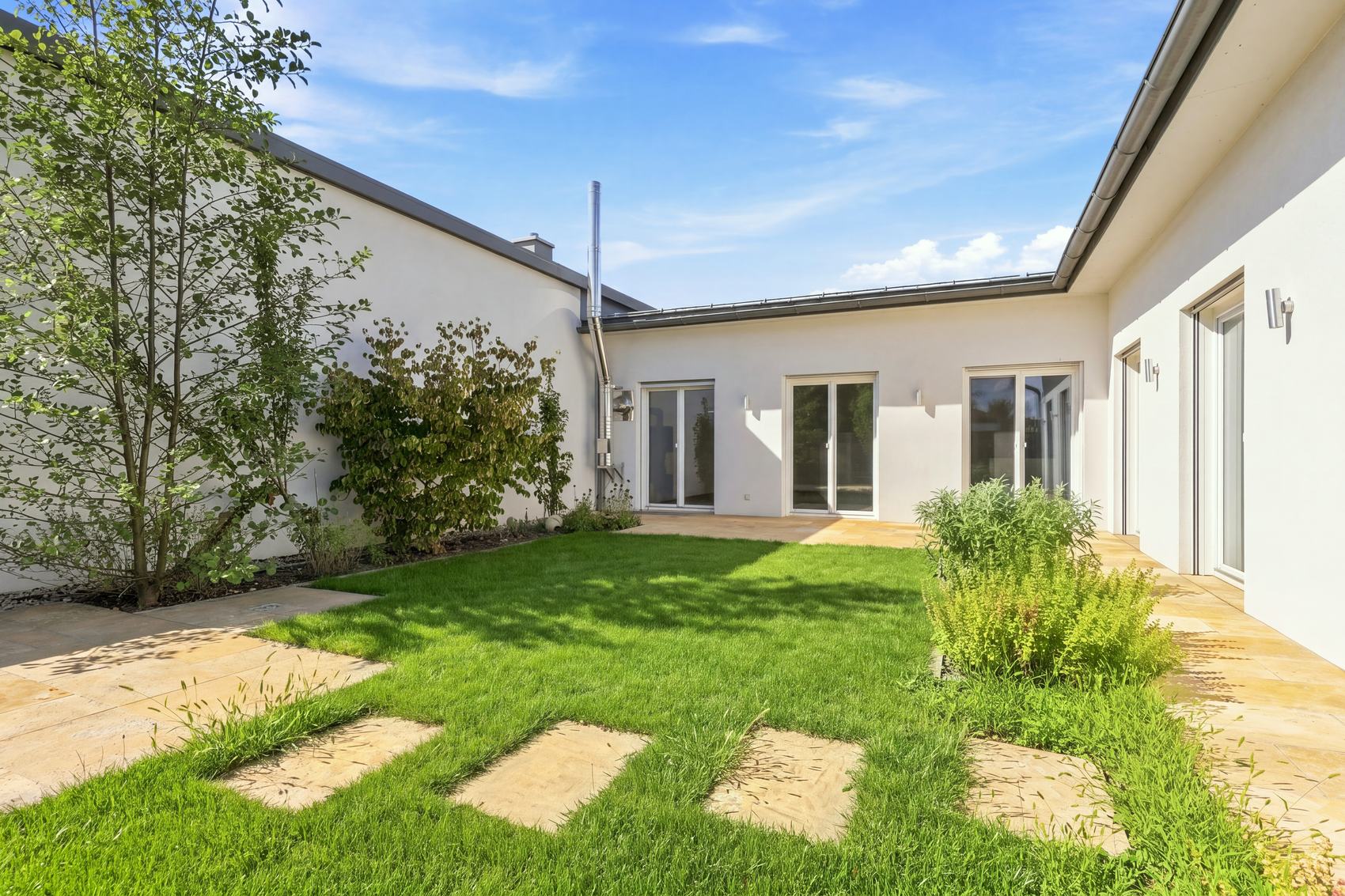 Innenhof eines Bungalows mit Rasen und Trittplatten unter blauem Himmel