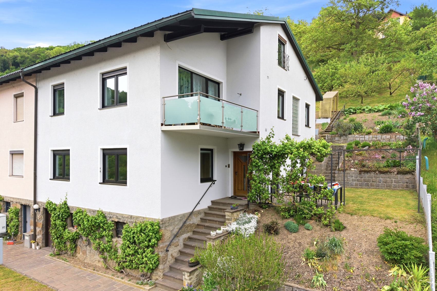 Weißes Haus mit Balkon und Garten am Hang