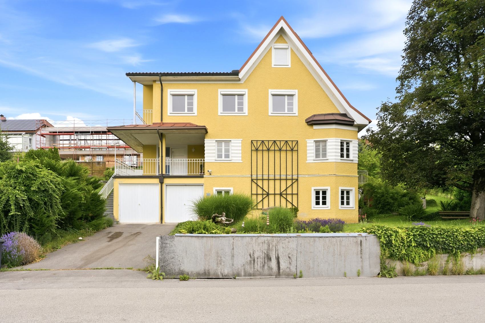 Gelbes Haus mit Erker und Balkon hinter einem Zaun