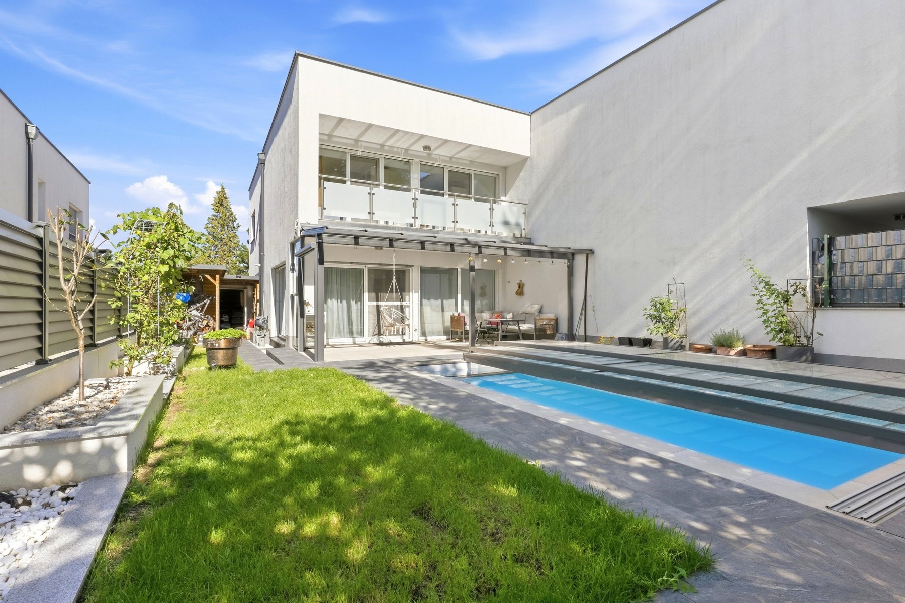 Weißes Haus mit Glasfront, davor Rasen und ein schmaler Pool mit Holzterrasse